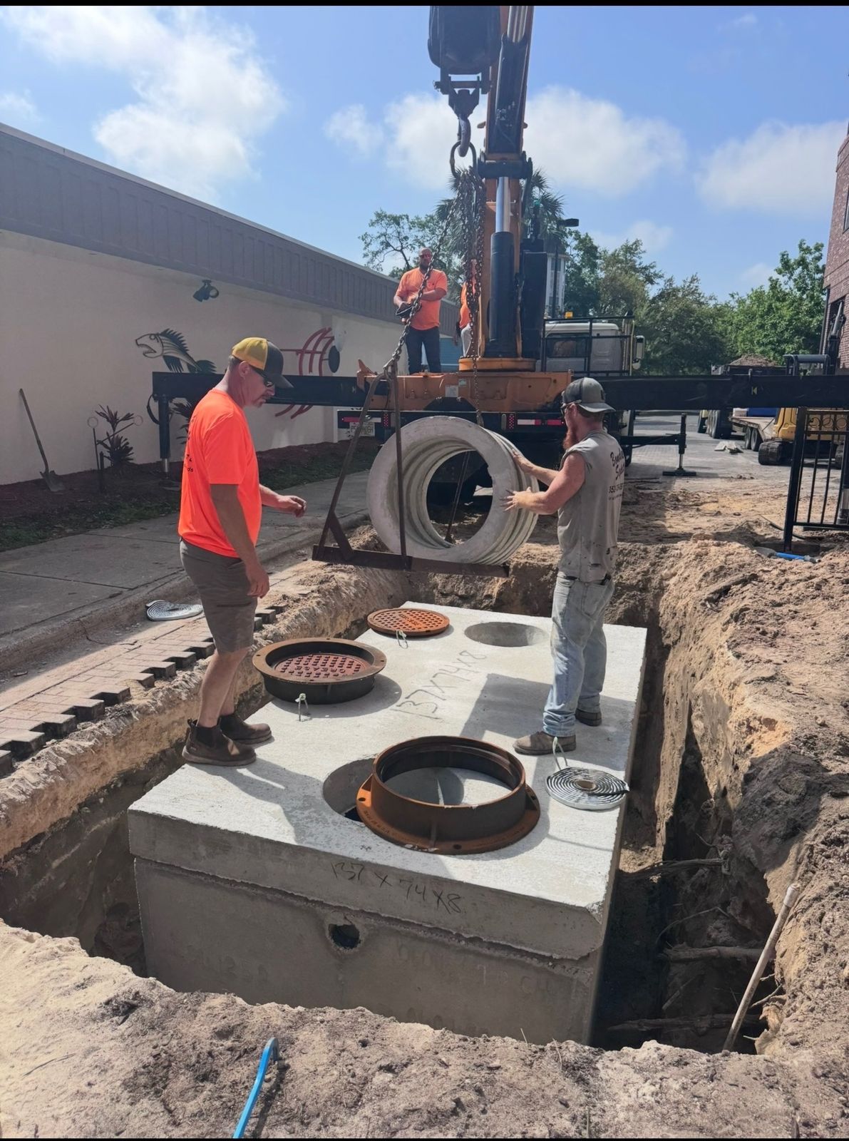 Crane setting a large precast concrete septic tank into an excavation on a commercial job site